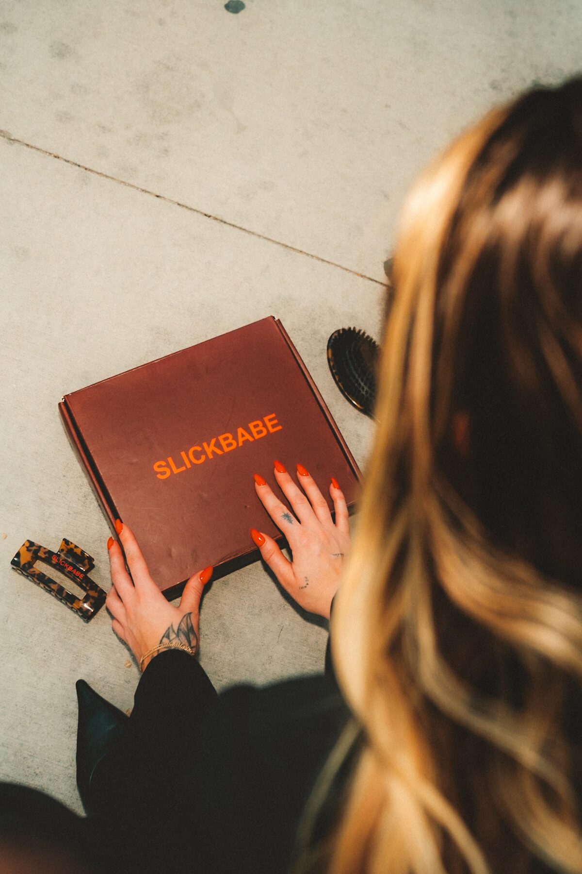 Hands on SLICKBABE branded box with Baby Hair BFF wand, tortoiseshell clips, and paddle brush — overhead product shot