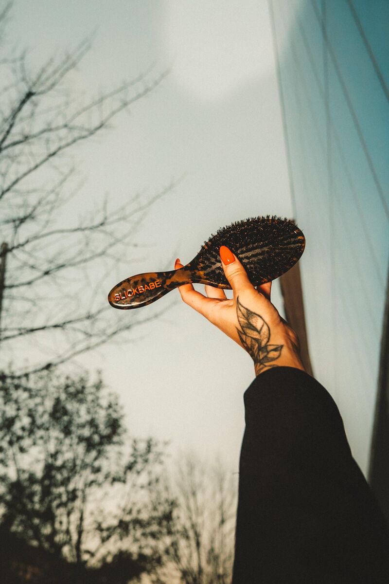 SLICKBABE paddle brush held up against sky — product editorial