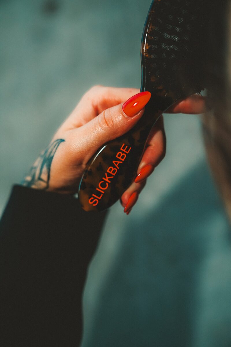 Hand brushing through hair with SLICKBABE tortoiseshell paddle brush — close-up product in use